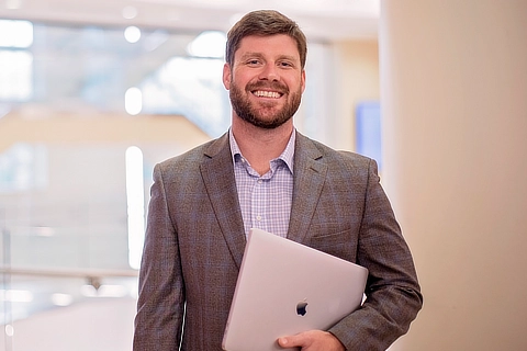 male business student standing with laptop in foyer