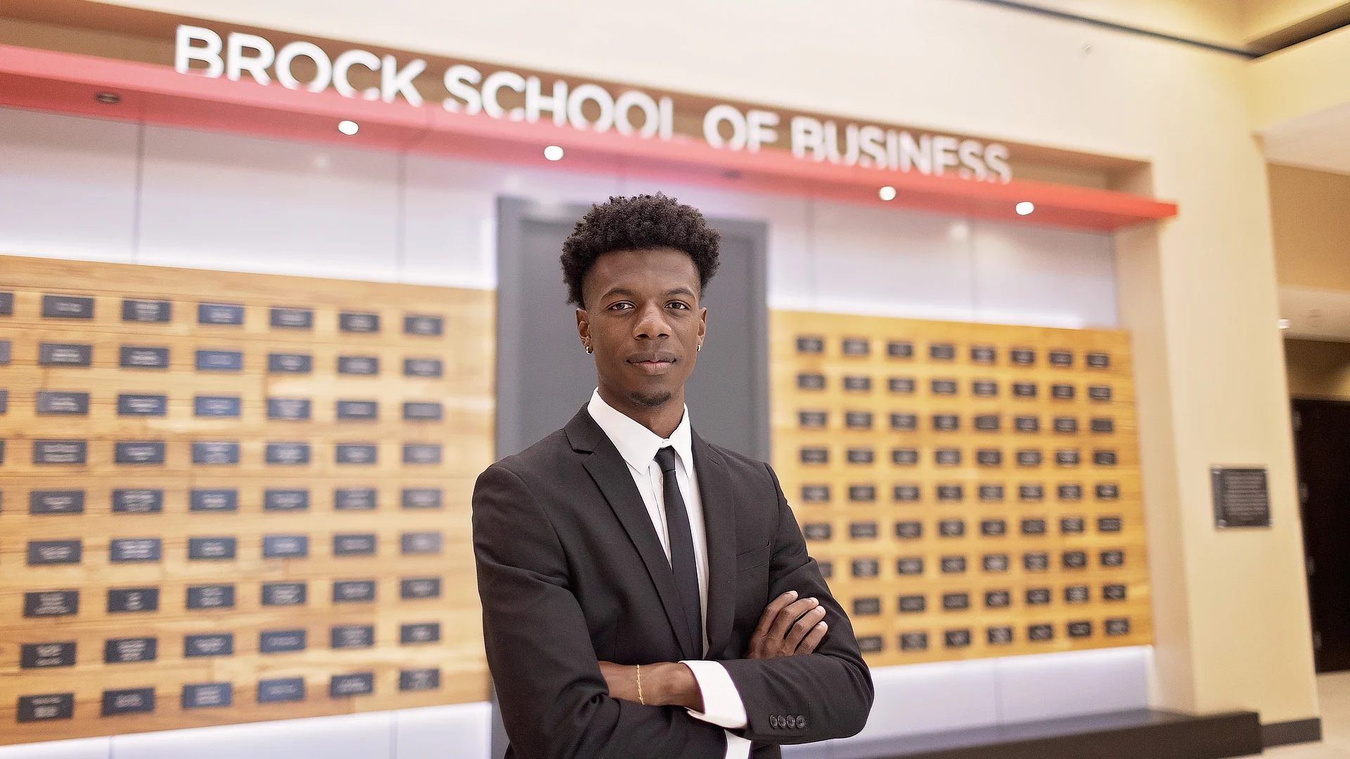 male student standing in front of the donors wall